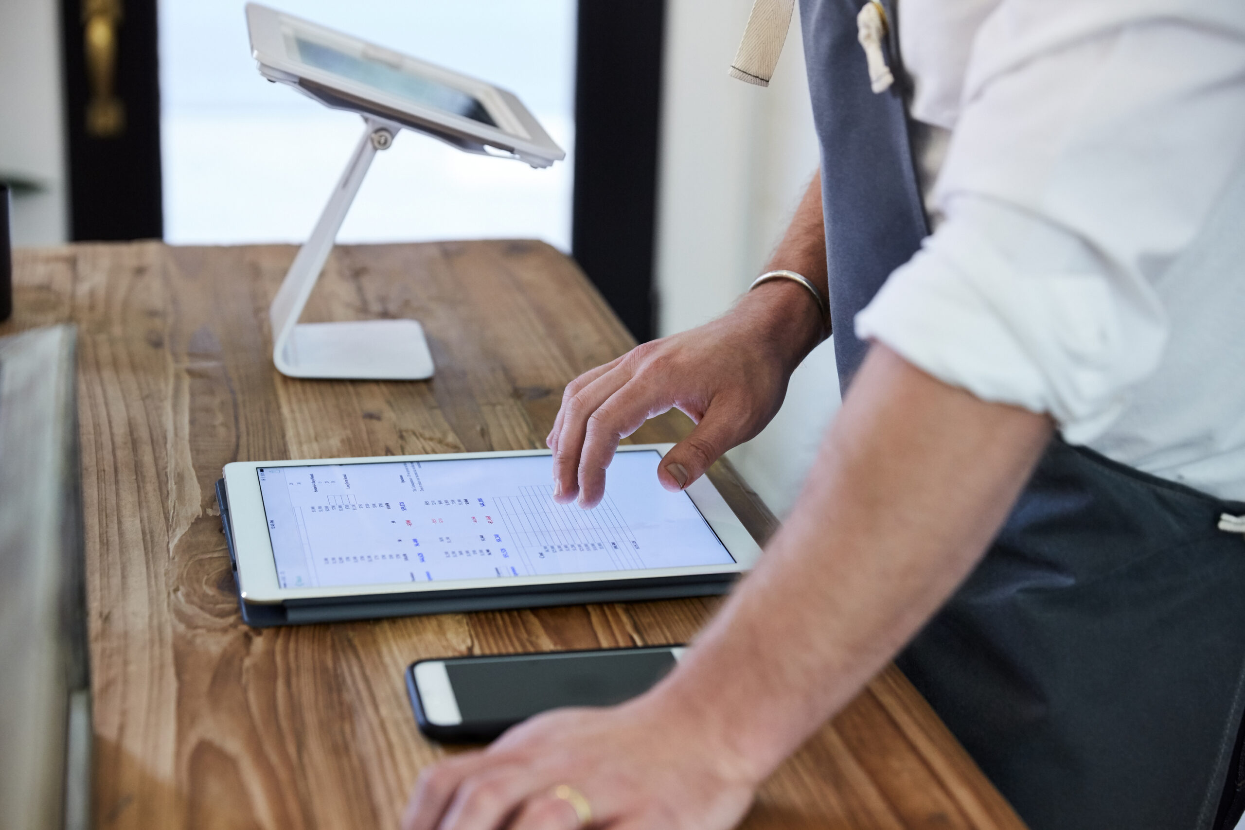 Person typing onto digital tablet with mobile phone sitting in front of them