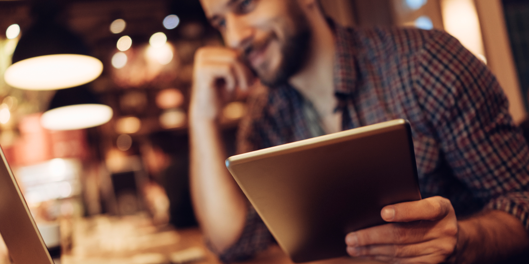 Man smiling while looking at computer screen and holding a tablet