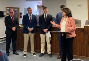 woman speaking at a podium with group of men behind her